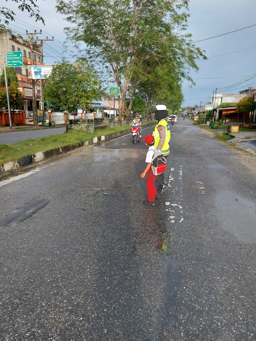 PEDULI KESELAMATAN – SATLANTAS POLRES SUBULUSSALAM BANTU SEBERANGKAN ANAK SEKOLAH